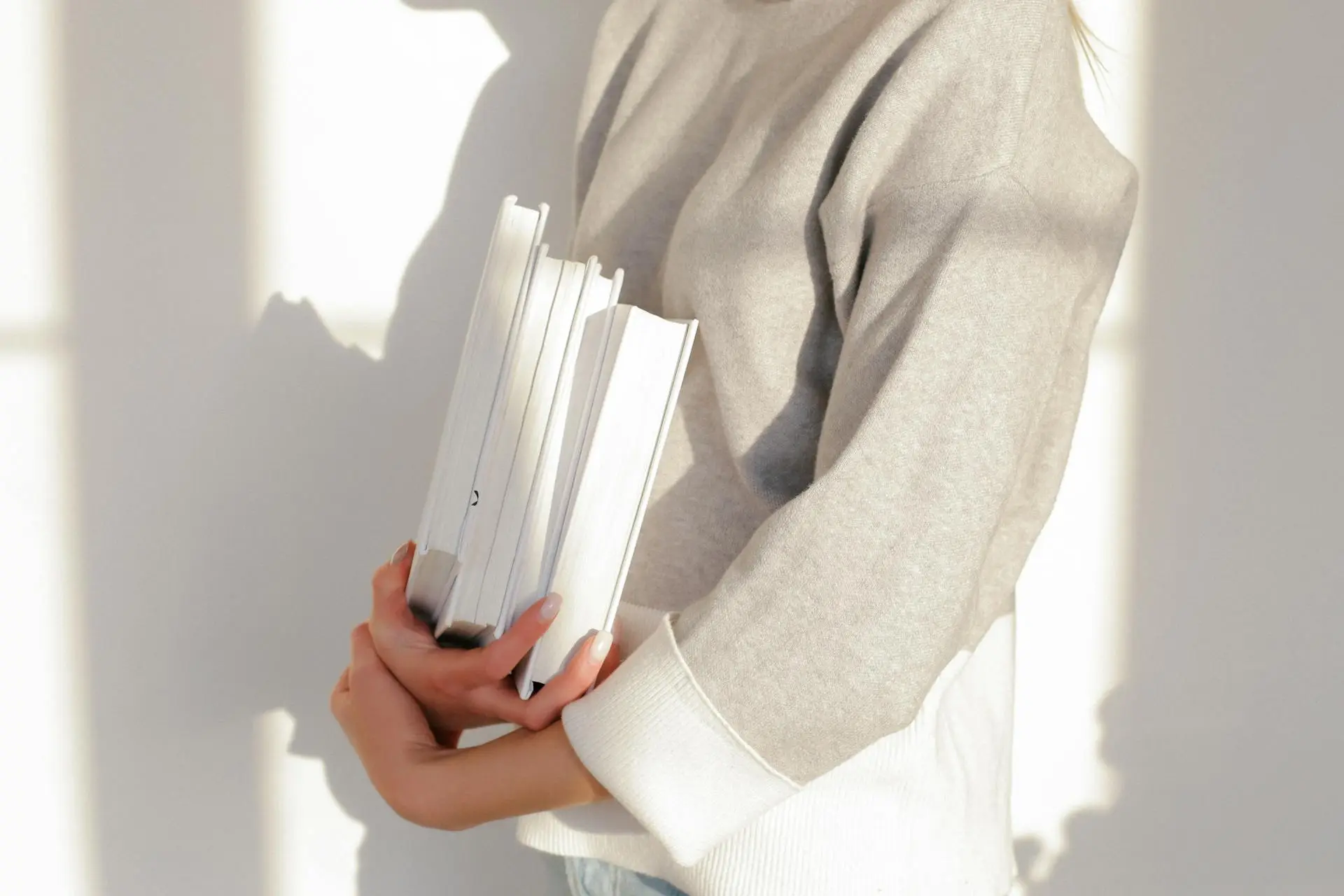 A person in a long-sleeved shirt holding several books with white covers and pages